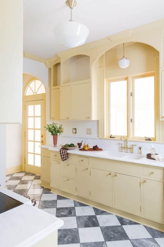 The Butter Kitchen with pale yellow cabinetry, brass hardware, and checkered marble floor