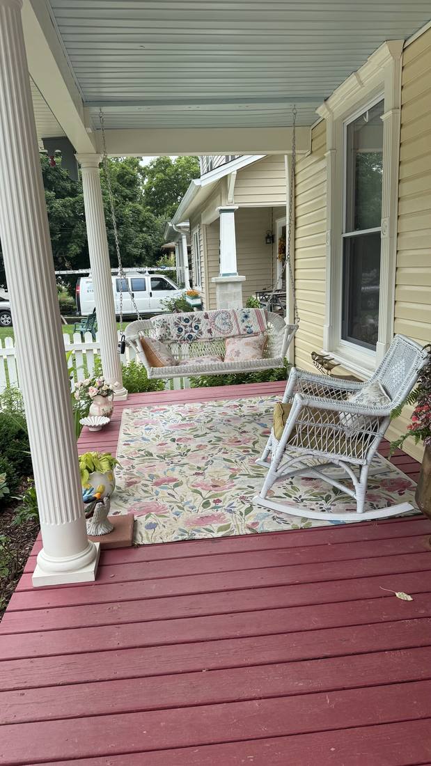 The front porch with a wicker swing, rocker, and floral rug