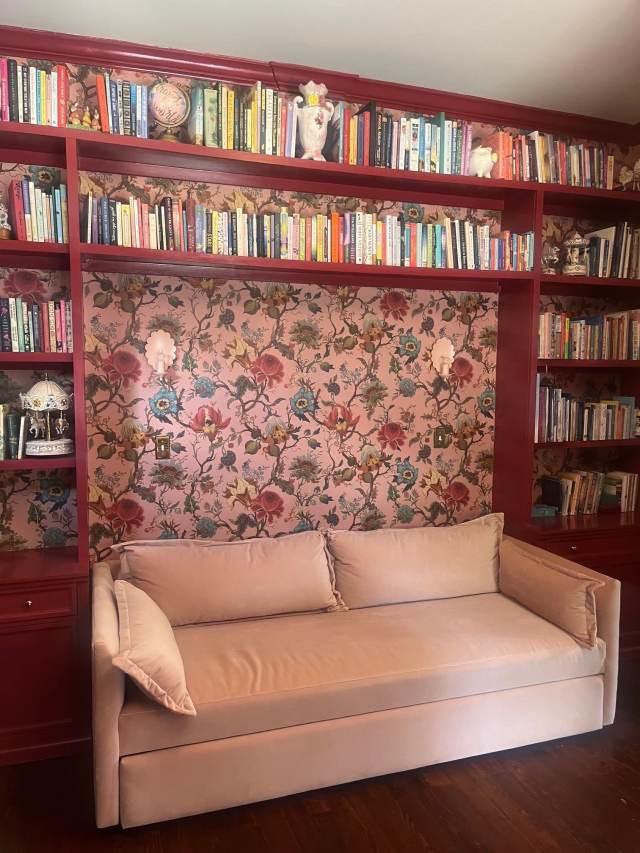 The Library with built-in crimson bookshelves, floral wallpaper, and a blush velvet sofa